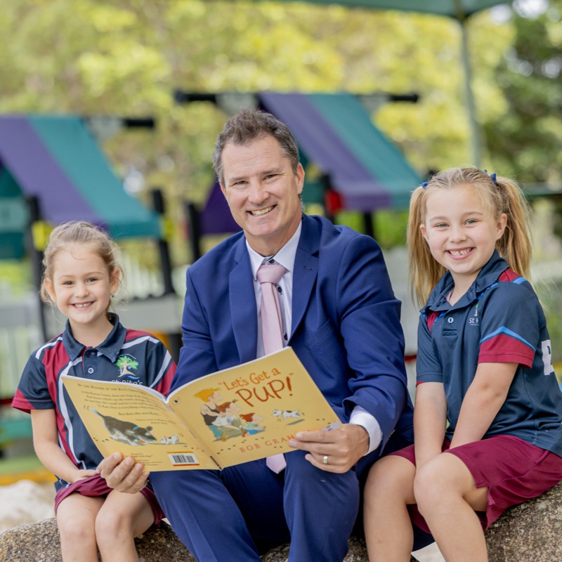 Staff member reading with students outdoors supporting literacy development and positive relationships within the school community